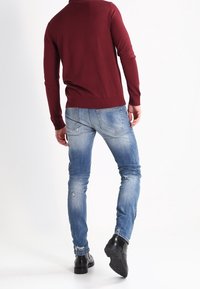 Maglione bordeaux a maglia con maniche lunghe, abbinato a jeans skinny azzurri chiari strappati e stivali neri alla caviglia.