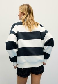 Felpa oversize a righe blu navy e bianche, con maniche larghe e texture morbida. Abbinata a pantaloncini di jeans scuri.