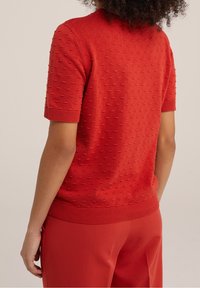 Röd kortärmad stickad topp med en strukturerad, bobble-mönster, ribbad halsringning och ärmslut, i kombination med matchande röda byxor.