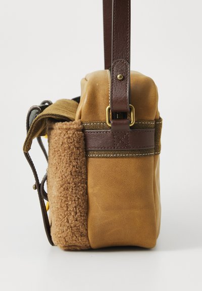 Geantă din piele maro cu o latură din fleece texturat, curea maro cu accesorii aurii și o formă rectangulară compactă.