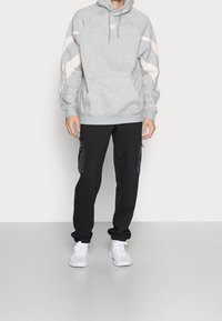 Grå hoodie med rosa detaljer och en känguruficka, ihop med svarta joggarbyxor med dragkedjefickor och vita sneakers.