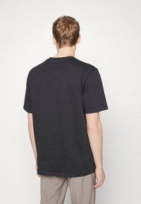 Tricou scurt cu mânecă neagră, din bumbac, cu decolteu rotund și o croială lejeră, afişat din spate pe un fundal alb simplu.