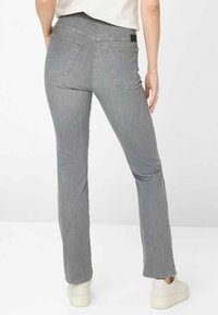 Szare, elastyczne dżinsy z rozkloszowanym krojem, posiadające dwie tylne kieszenie i czarną talię, stylizowane z białymi sneakersami.