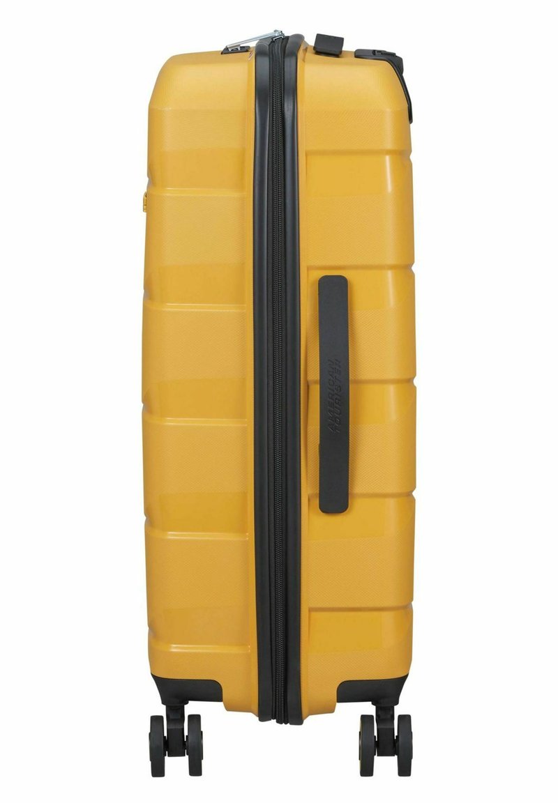 Gele harde koffer met gestructureerde oppervlakte, zwarte rits en een zijhandvat. Vier wielen voor mobiliteit. Slank, rechthoekig ontwerp.