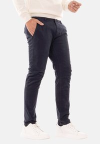 Pantaloni in cotone navy con vestibilità slim, dotati di tasche laterali e parte anteriore piatta. Abbinati a sneaker bianche a basso profilo.