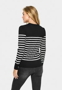 Maglione a righe bianche e nere con maniche lunghe, polsini a costine e vita aderente, mostrato da dietro, abbinato a jeans scuri.