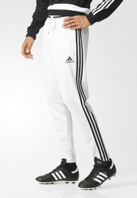 Vita idrottsbyxor i mjukt material, med två svarta sidostrecker, dragsko i midjan och en Adidas-logga på låret.