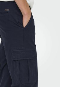 Marinefarbene Cargo-Hosen mit Seitentaschen, schräge Fronttaschen und einem Stoffbund. Das Material wirkt strapazierfähig mit einer glatten Textur.