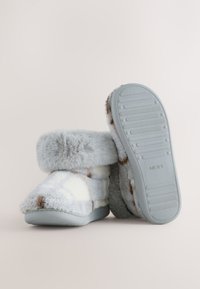 Grau-weiße, flauschige Hausschuhe mit einem weichen Bündchen, gemustertem Muster und Gummisohlen mit rutschfestem Design. Markenlogo auf der Sohle.