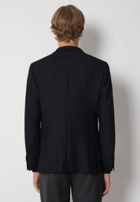 Blazer azul marino con un ajuste entallado, hombros estructurados y abertura simple en la parte posterior. Presenta puños abotonados y una textura de tela suave.