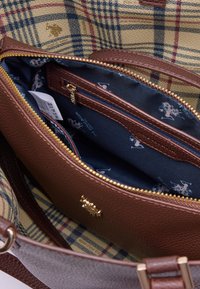 Interno di una borsa in pelle marrone testurizzata con una fodera blu navy, dotata di una tasca con zip e hardware dorato. Il motivo a quadri è visibile all'esterno.