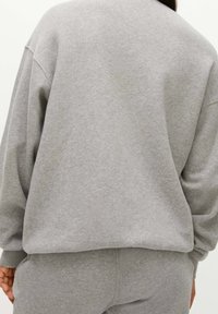 Felpa grigia con una vestibilità rilassata, realizzata in morbido cotone. Presenta spalle scese e polsini a costine, vista da dietro.