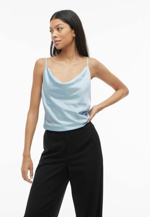 Top de satén azul claro con escote drapeado y tirantes finos, combinado con pantalones de pierna ancha negros, que presentan una textura suave y un corte relajado.