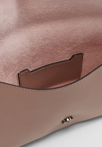 Beige läderhandväska med en mjuk rosa foder, med en tanfärgad ficka och en metallknäppning. Slät textur över hela.