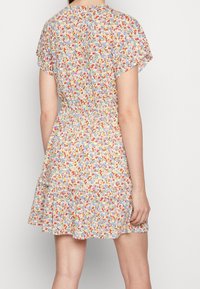 Robe à imprimé floral avec manches courtes évasées, taille élastiquée et ourlet à volants superposés. Présente un fond blanc avec des fleurs colorées.
