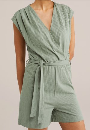 Combinaison-short sans manches vert sauge texturé, avec encolure en V et ceinture en tissu nouée à la taille, portée par une personne debout.