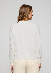 Ljus beige tröja med långa ärmar, ribbad halsringning och muddar. Mjuk textur, avslappnad passform och en nederkant som sitter vid midjan.