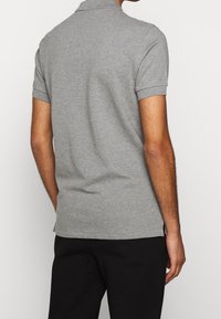 Graues Poloshirt mit kurzen Ärmeln und Kragen, aus einem Baumwollmischgewebe gefertigt. Hat einen geraden Saum und gerippte Ärmelabschlüsse.