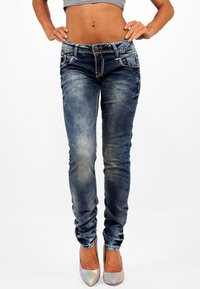Vaqueros ajustados de color azul con secciones desteñidas y costuras en contraste. Presenta bolsillos y una cinturilla de altura media. Combinado con tacones puntiagudos y brillantes.