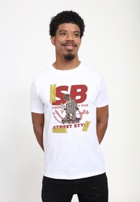 Bílý bavlněný tričko s grafikou kreslené postavičky na kolečkových bruslích, s tučným červeným a zlatým textem "SB TWENTY FIVE STREET STYLE."