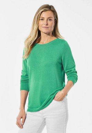 Groene trui met een ronde hals en lange mouwen, gemaakt van zachte stof. Gecombineerd met witte broek, met een relaxte pasvorm.