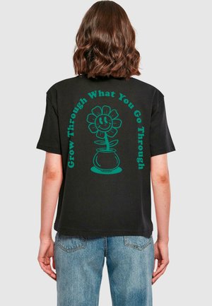 Black cotton t-shirt featuring a turquoise flower graphic and text "Grow Through What You Go Through" printed on the back.