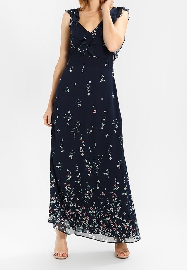 Navy maxi jurk met bloemenpatroon, ruches op de schouders, V-hals en doorschijnende zoom. Lichtgewicht materiaal en vloeiende uitstraling.