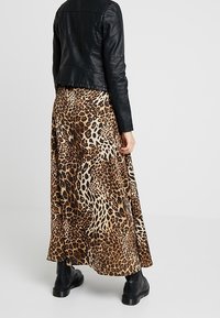 Maxi gonna con stampa leopardata realizzata in tessuto morbido, caratterizzata da un design fluido con uno spacco alto, abbinata a una giacca di pelle nera e stivali.