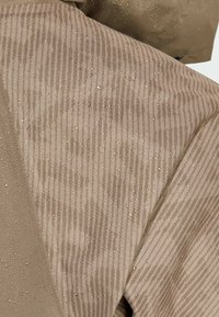 Water-resistant brown jacket fabric with vertical stripes and textured surface, featuring visible water droplets on the material.