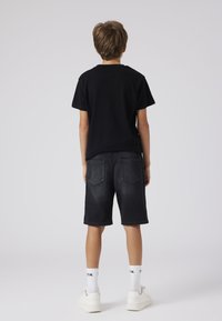 Juoda medvilninė marškinėliai derinami su tamsiais džinsiniais šortais, turinčiais dvi galines kišenes, ir baltais sportbačiais su raštuotomis kojinėmis. Paprastas, kasdienis aprangos derinys.