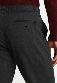 Pantaloni neri strutturati con una tasca posteriore con bottone, cintura elastica e design slim fit.