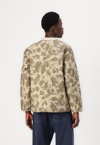 Quilted jakke i beige med camouflage mønster, med rund hals, lange ærmer og en afslappet pasform. Lavet af glat stof.