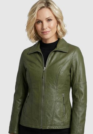 Woman with short blonde hair wearing a fitted olive green leather jacket zipped over a black top against a plain light background.