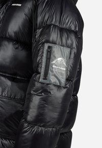Černá lesklá prošívaná bunda s rukávem, zipovou kapsou a logem "PEGADOR Outerwear" s motivem hory.