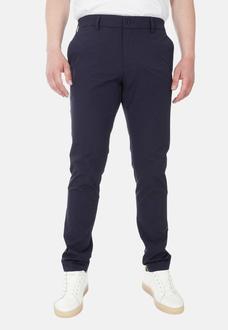 Pantaloni slim-fit blu navy con frontale piatto, passanti per cintura e chiusura con bottone. Realizzati in tessuto liscio, abbinati a sneakers bianche.