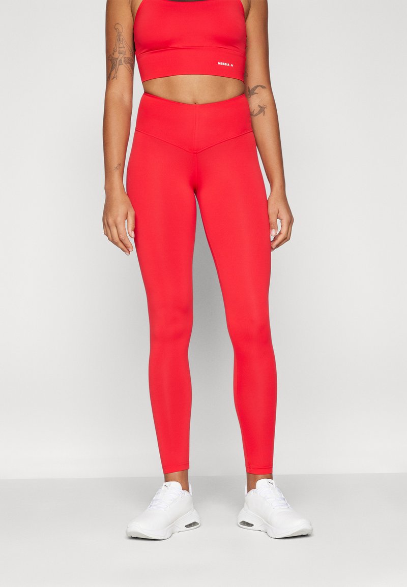 Leggings sportivi rossi realizzati in tessuto elastico con vita alta. Abbinati a un crop top coordinato e scarpe da ginnastica bianche.