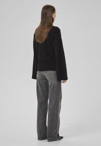 Pulover negru supradimensionat cu mâneci largi, purtat cu blugi închiși la culoare, lejeri. Design simplu, fără modele vizibile sau accesorii.