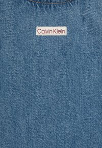 Denimtyg i ljusblått, med en Calvin Klein-logotyp i rött på en vit bakgrund. Slät struktur med fint, subtilt sömnad.