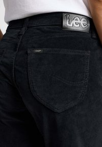 Svarta kordflorsbyxor med en texturerad yta, med en läderetikett i midjan som säger "Lee" och en liten etikett på bakfickan.