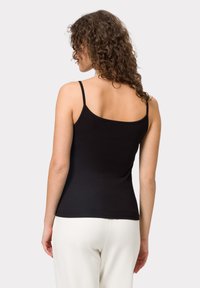 Zwarte camisole met dunne bandjes, zachte stof, aansluitend ontwerp, ronde halslijn en gladde textuur, gedragen met lichte broek.