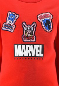 Red fabric with Marvel Superheroes text and patches of Captain America, Thor, and Black Panther faces with names on the chest area.