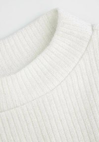 Biały prążkowany sweter z teksturowaną powierzchnią i zaokrąglonym kołnierzem. Wzór dzianiny jest wyraźny, pokazując różnice w grubości.