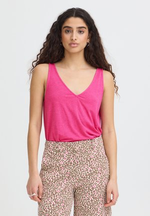 Donna con capelli lunghi e ricci che indossa un top rosa senza maniche con scollo a V e pantaloni beige a vita alta con stampa leopardata rosa e marrone.