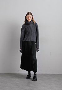 Sweater de malha canelada cinza escuro com um alto gola alta, combinado com uma saia longa preta plissada e botas pretas de tornozelo.