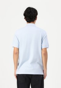 Γαλάζιο πόλο πουκάμισο, με θέα από πίσω, διαθέτοντας γιακά, κοντά μανίκια και χαλαρή εφαρμογή. Λείο ύφασμα, απλός σχεδιασμός.