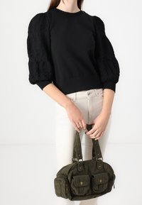 Svart sweatshirt med texturerade puffärmar, rund halsringning, kombinerad med en mörkgrön kordflugeväska med två framfickor och bärremmar.