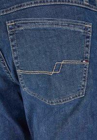 Poche arrière en denim avec des coutures jaunes, présentant un design géométrique. Le tissu est d'un bleu moyen avec une texture lisse et un léger dégradé.