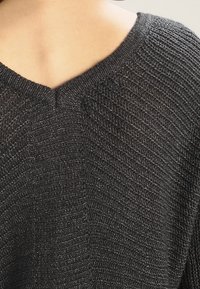 Maglione nero a maglia con scollo a V, tessuto textured e una vestibilità leggermente ampia, con cuciture visibili e collo a costine.