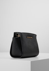 Černá kožená kabelka se strukturovaným designem, s zlatým logem "MICHAEL KORS" a texturovaným povrchem. Kompaktní a štíhlá.