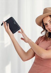 Black zip-around wallet made of textured material with a hexagonal pattern and subtle logo detail; held in a hand against a light background.